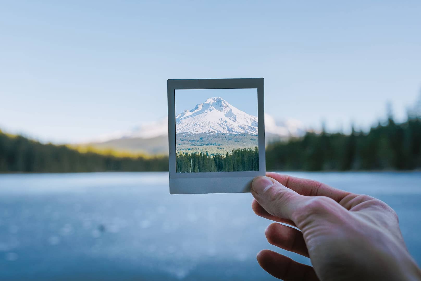 person holding a polaroid picture of snow covered mountain